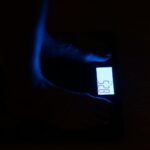 Close-up of a digital weighing scale displaying weight in a dark room with blue illumination.