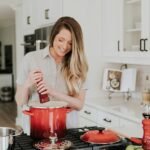 smiling woman standing and putting pepper on stock pot